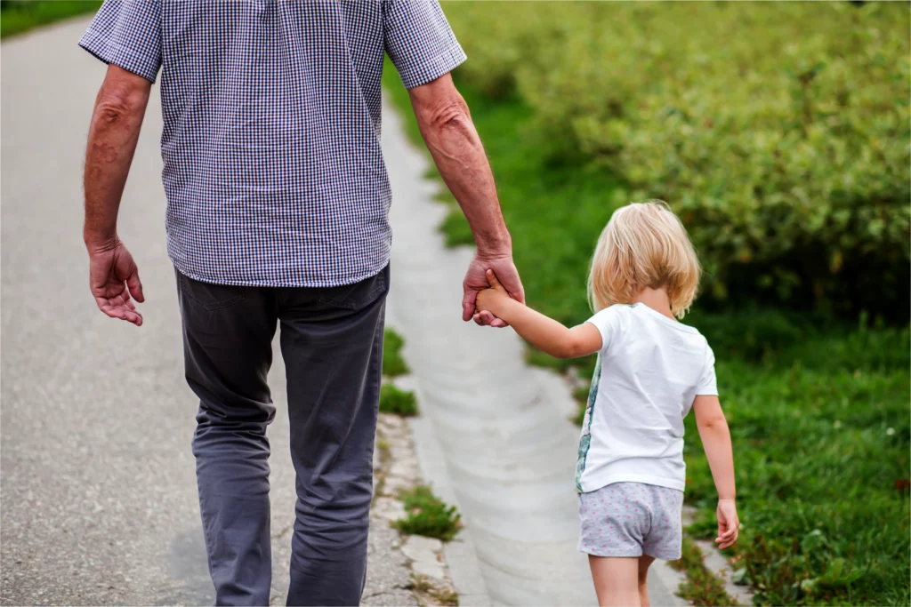 Elderly man holding a young childs hand walking